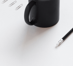 A mug of coffee on a desk next to a pencil and paper clips