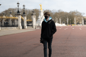 Man in a black coat and a Covid mask walking around Buckingham palace