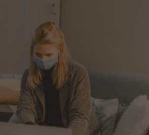 Blonde woman in a covid mask working on a laptop